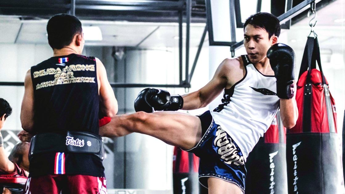 A man throwing a Muay Thai round house kick at the gym.