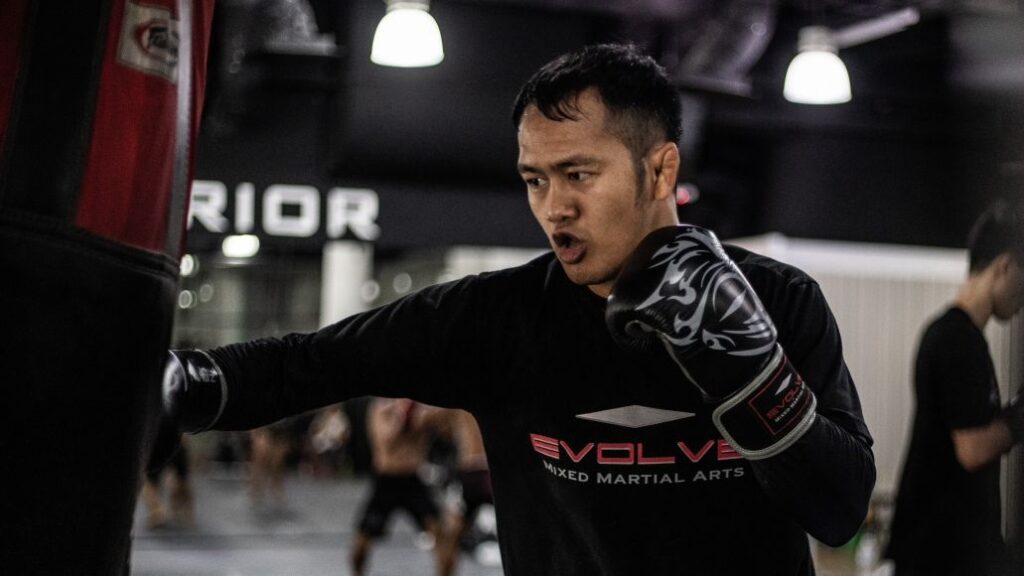 A Muay Thai fighter throws a hook punch on a heavy bag.